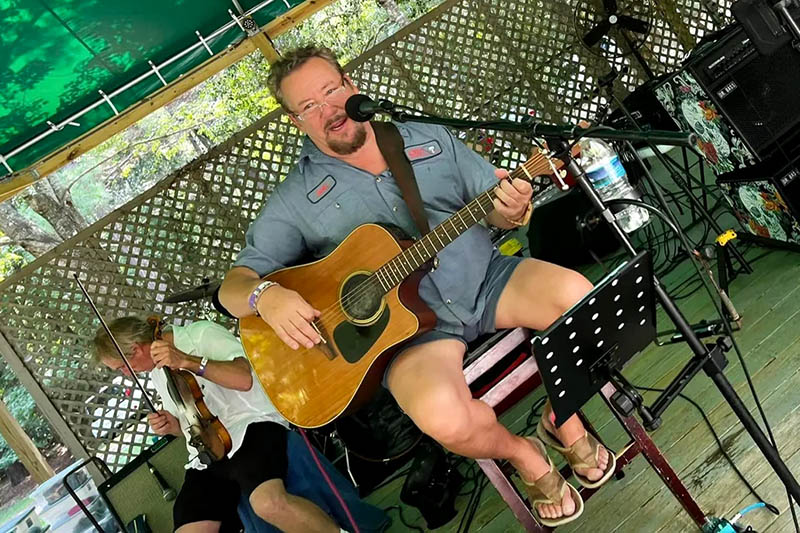 Angled photo of Paul Grimshaw playing guitar and singing