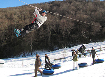 Snow tubers at Hawksnest in North Carolina watch as someone ziplines above the snow tubing lanes.